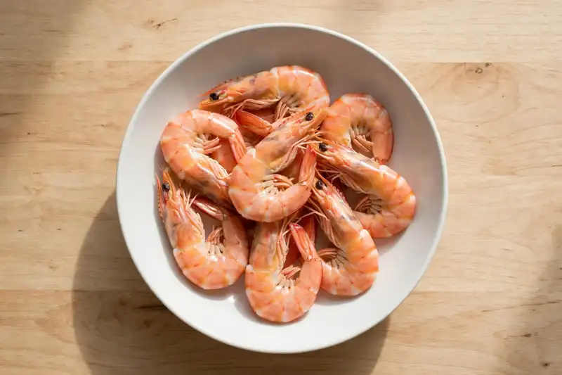 Plain steamed shrimp in a white bowl, fully cooked with no seasoning